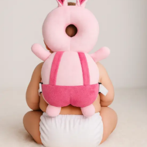 Baby wearing Pink Uv bunny head protector cushion while sitting on floor